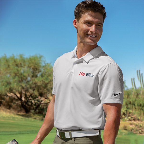 Man smiling outdoors in a white NMA-branded polo shirt